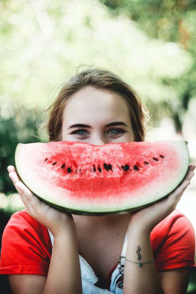 A person holding up a large slice of watermelon in front of their space as if a smile