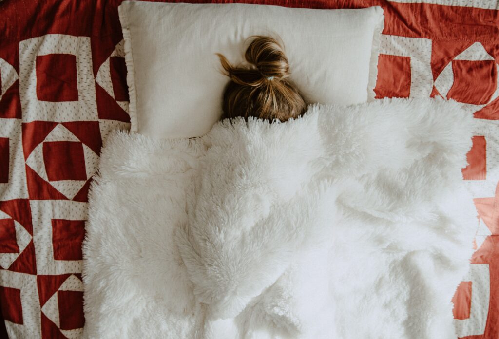 Person lying on patterened bed-spread.Only see top of head on white pillow with rest covered with blanket