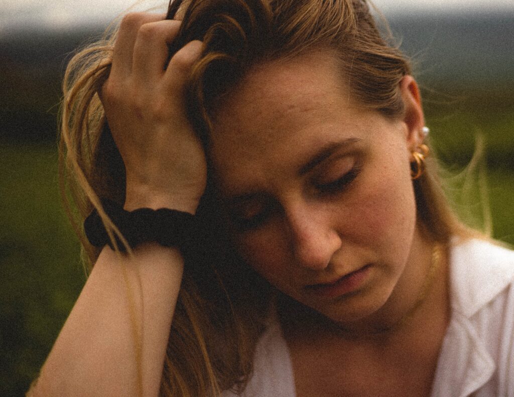 Woman in white top an blck watch holding her heard with right hand.