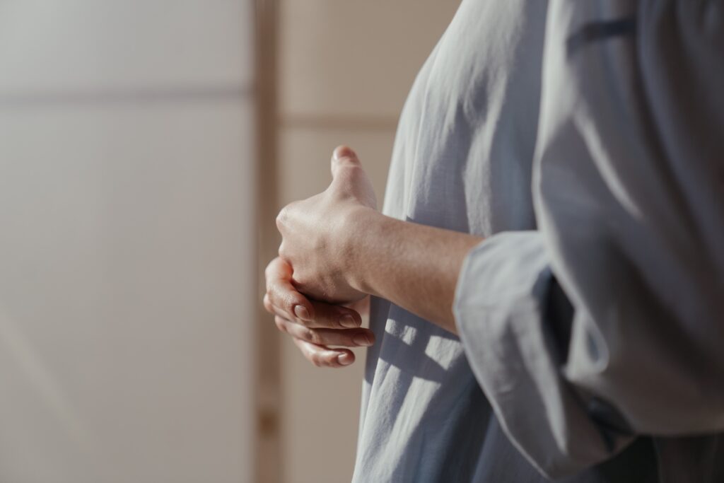 Side view of person with arms across body wringing their hands