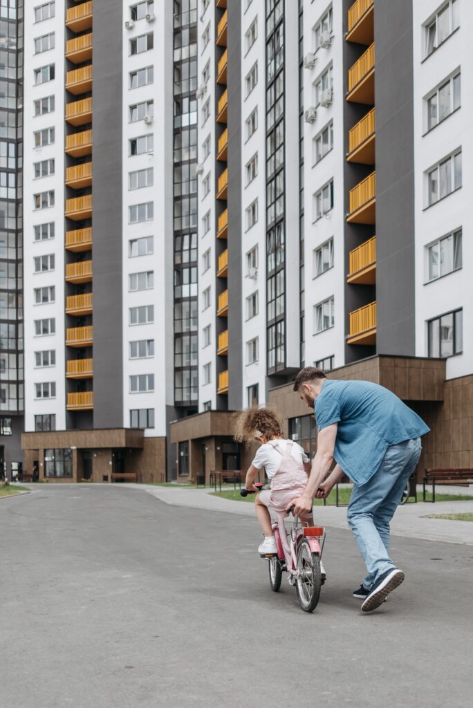 Father teaching daughter how to ride a bicyle in front of a block of flats.