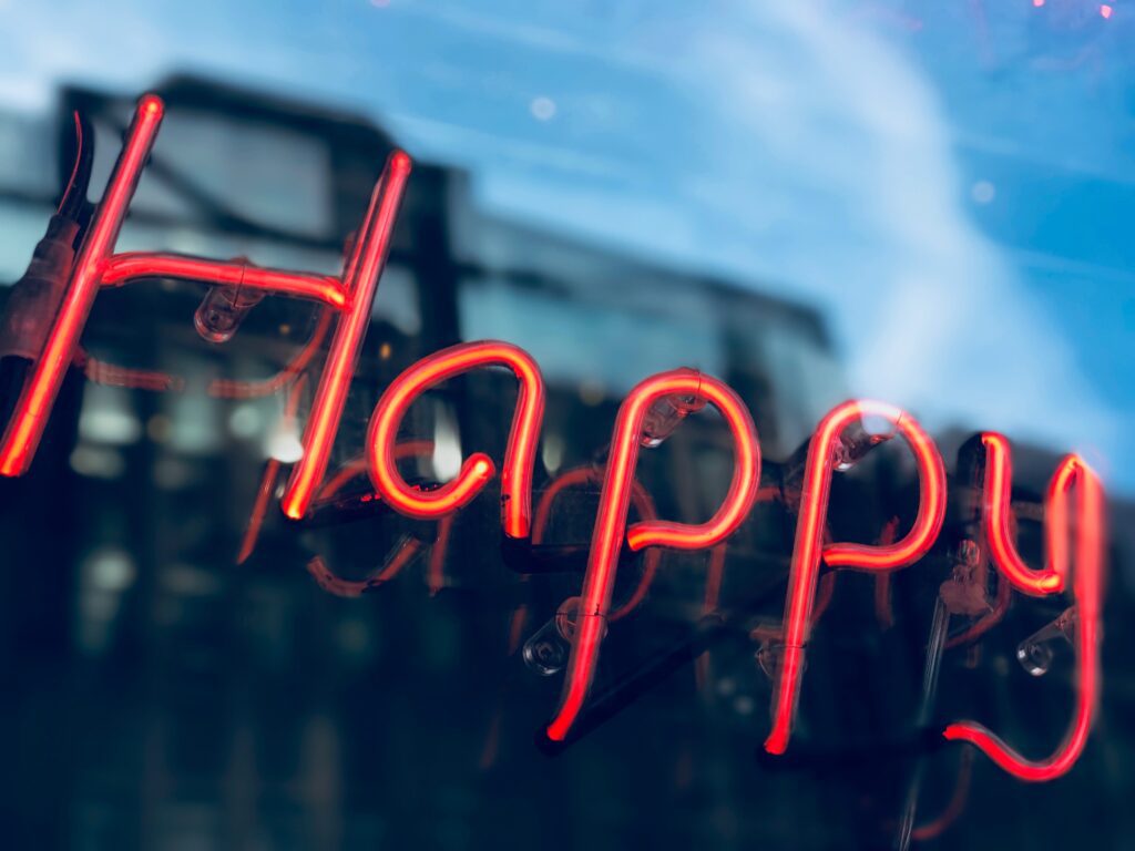 'Happy' in red light neon piping in a window with reflection.