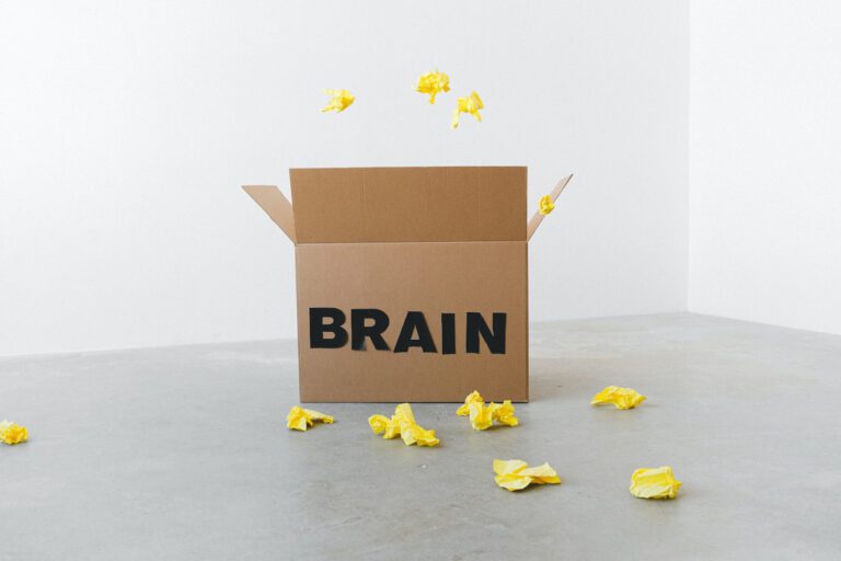 A brown cardboard box with with word 'BRAIN' printed on it and scrunched up pieces of yellow paper flying from the box and littering the floor around the box.