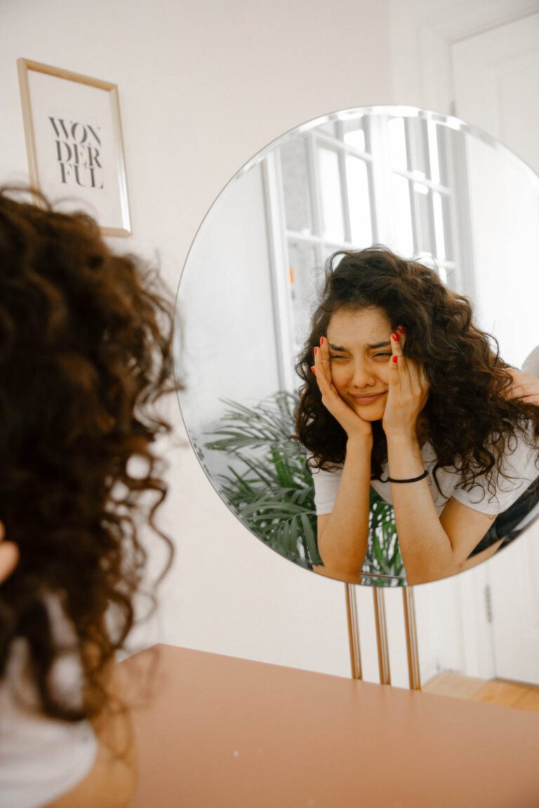 A person looking at themselves in a mirror while crying. Another supporting them with a hand on their shoulders